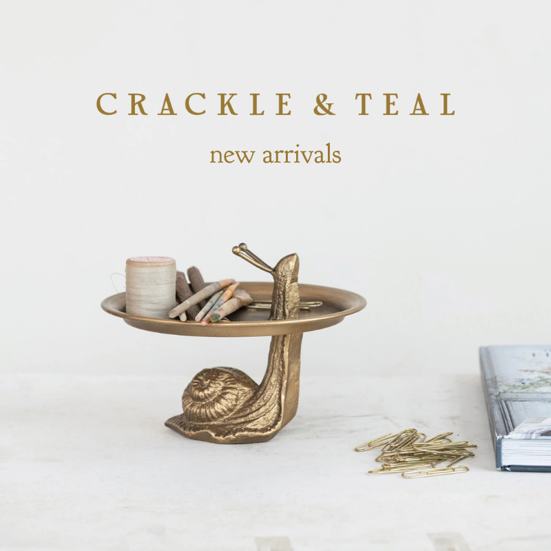 Brass snail-shaped pedestal tray holding spools of thread, small trinkets, and decorative items, set on a neutral surface. A stack of books and scattered gold paper clips are nearby. Overlay text reads 