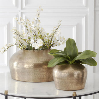 Artificial orchid stems and leaves styled in hammered brass pots. 