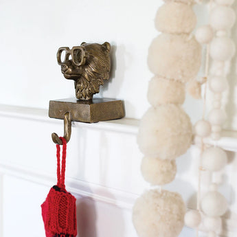 Antique brass bear stocking hanger in gold finish on a white painted mantle holding a knitted red stocking.