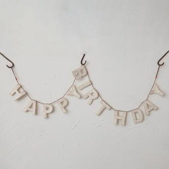 Happy Birthday Wool Felt Garland string along a roman clay finished wall. 