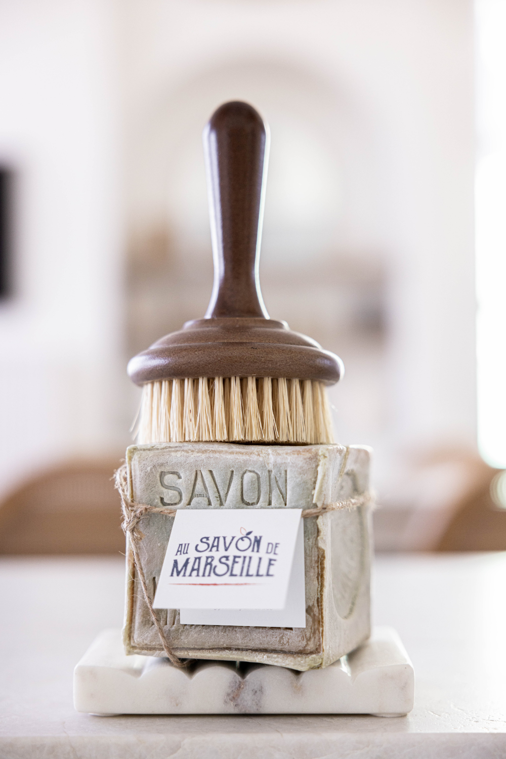 Dish Soap Scrub brush with dark wood handle sitting on top of a cube of household soap by Savon de Marseille.