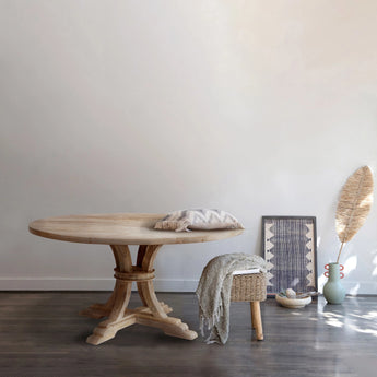 The Mango Wood Pedestal Dining Table in a home styled with a seagrass stool, cushions and throws. 