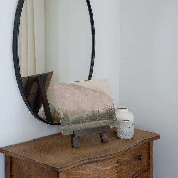 Mountain Pine Artist Board sitting on a dark wood easel in a bedroom on an antique dresser. 