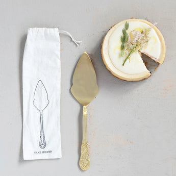 Brass Cake Server in Printed Drawstring Bag styled with a small cake. 