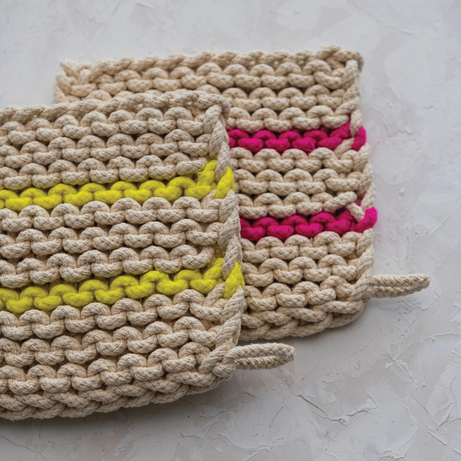 Two cotton pot holders sat on top of eachother, one with a pink stripe and one with a yellow stripe.