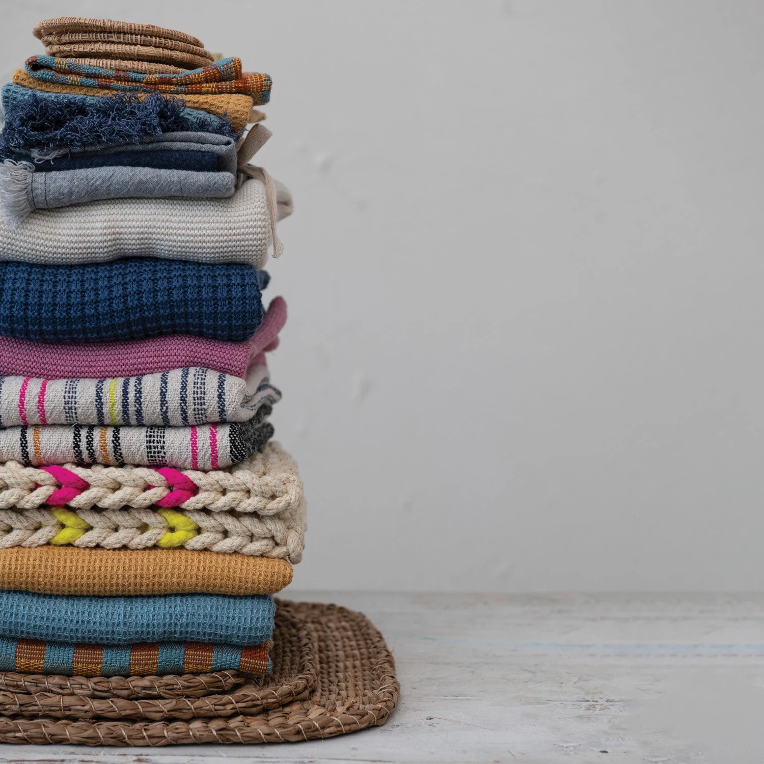 Crochet pot holders blended in with a stack of various kitchen items such as tea towels and trivets. 